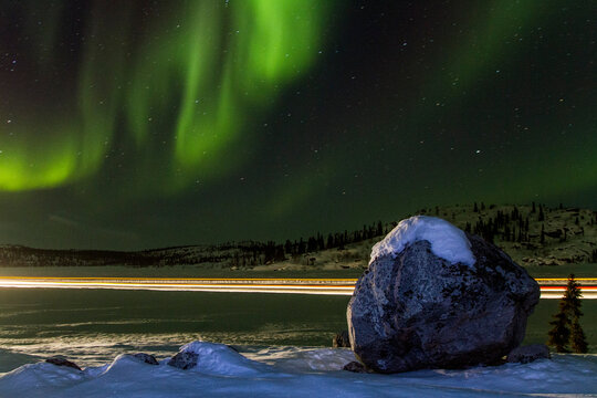 Long exposure of Jeep lights trails under the Aurora Borealis over Great Slave Lake in Northwest Territories, Canada