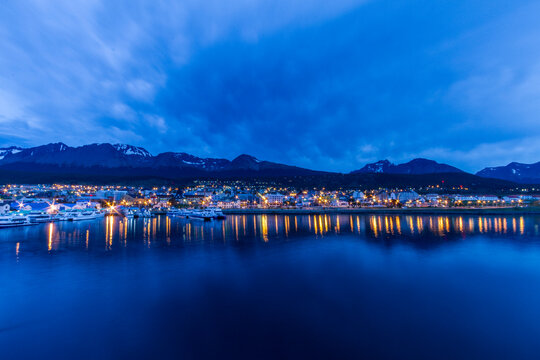 Night lights reflect on water in Ushuaia, the southernmost city in the world, showcasing the beauty of Tierra del Fuego