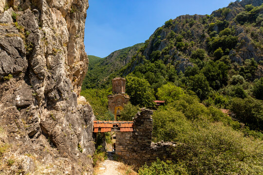 Stone pathway leads to old church remnants in Matka Canyon surrounded by mountains and greenery