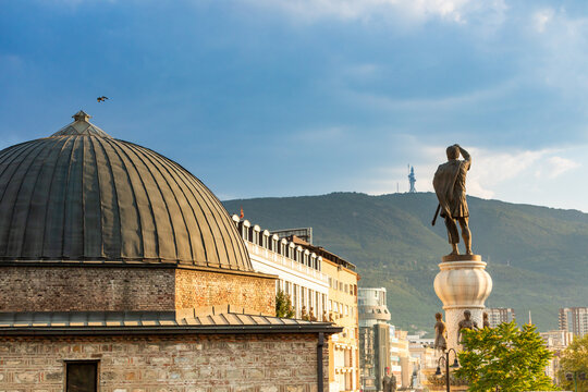Stone building with dome and statue of man holding sword in Skopje against mountain backdrop