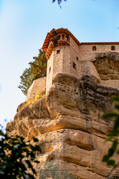 View of a stone monastery tower on a rock cliff illuminated by sunlight against a blue sky in Meteora, Greece