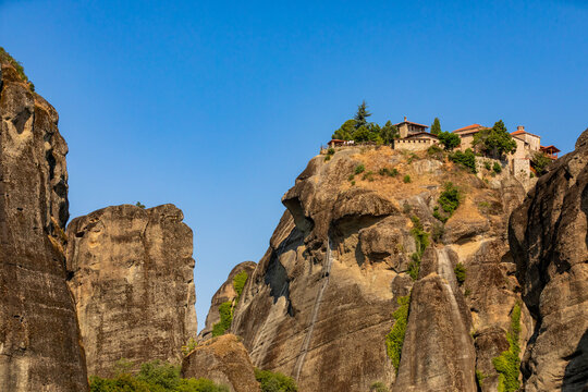 Monastery on high rock formation surrounded by cliffs under clear sky in Greece