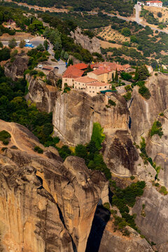 Aerial view shows Meteora monastery on steep rock in green landscape with distant buildings in Thessaly Greece