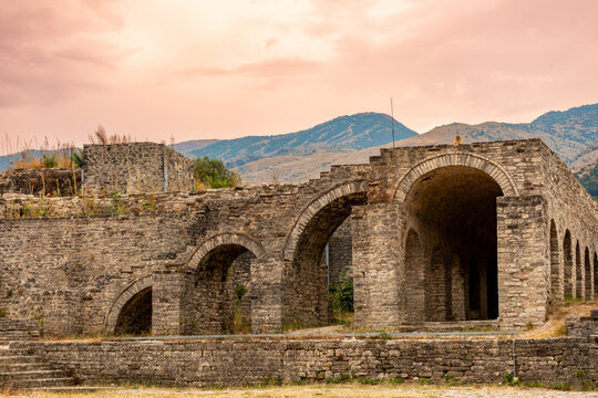 Sunset view of stone archways at Gjirokastr Castle with mountains and warm sky tones in Gjirokaster, Albania