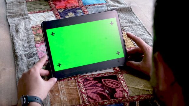 Hands holding a large tablet in horizontal orientation with green screen chroma key for movie watching or website demonstration while sitting outdoors during a sunny bright day