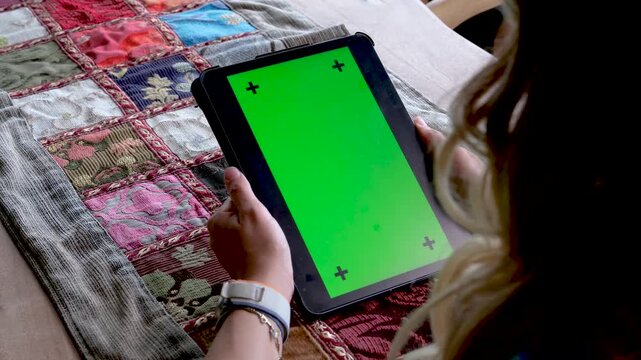 Close up of hands holding a smartphone in horizontal orientation with green screen chroma key and markers for video app or game demonstration over a traditional colorful rug