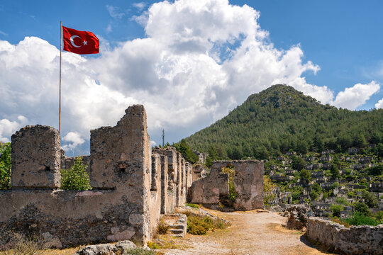 Turkish flag waves over the ruins of Kayakoy ghost town surrounded by lush mountains in Turkey