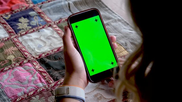 Close up of woman hands holding a smartphone with green screen chroma key in vertical orientation for social media app or vertical video demonstration at home during daytime