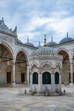 Yeni mosque courtyard shows stone fountain with arches and domes under cloudy sky in Istanbul, Turkey