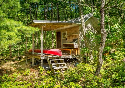 Red canoe resting in a cottage outbuilding surrounded by trees in Ontario, Canada on Francis Island