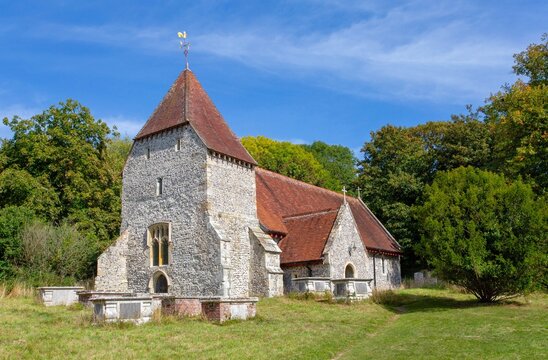 Unique spire of All Saints Church in West Dean, set against a bright blue sky and surrounded by greenery in East Sussex