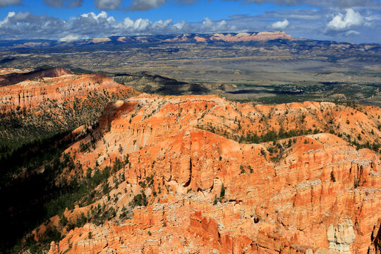 Views from a high point in Bryce Canyon reveal red rock formations and distant mountains under a bright sky in Utah