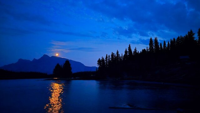 Moonlight reflects on Jack Lake with mountains and trees in the background near Banff, Alberta, Canada