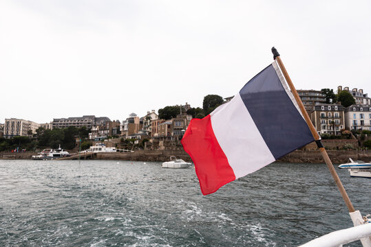 French flag waves on a boat as it leaves Dinard, showing Breton buildings across the water in Brittany France