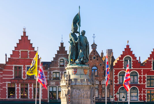 Statue in Markt during sunset with flags and historic buildings in Bruges, Belgium