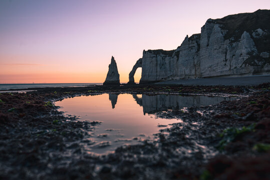Chalk cliffs and natural arch reflect in tidal pool at sunrise on the Normandy coast of France