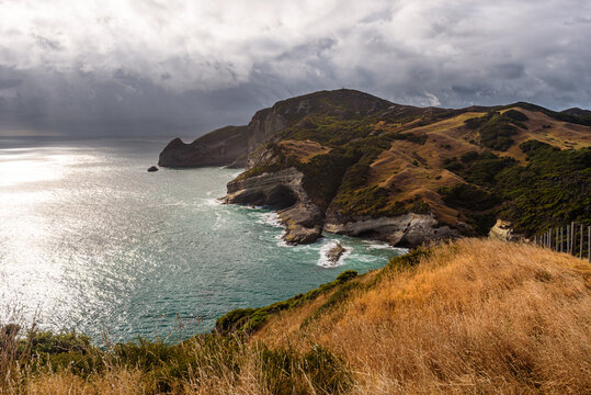 Rugged cliffs meet ocean waves at Cape Farewell on the South Island of New Zealand during cloudy weather