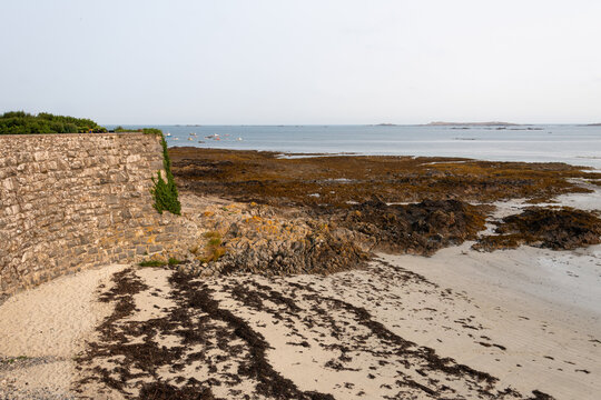 Coastal stone wall meets sandy tidal flats at Rocquaine Bay in Guernsey, Channel Islands during low tide in early evening light
