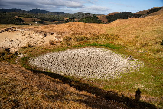 Arid farmland with dried pond and golden grass hills during summer drought in New Zealand