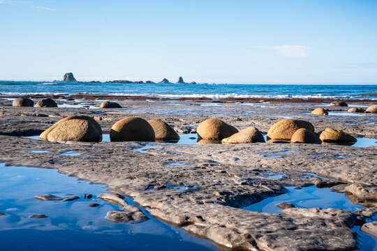 Rounded boulders on Cape Foulwind beach at low tide near Tasman Sea and West Coast cliffs in South Island New Zealand