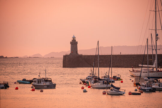 Golden hour at Saint Peter Port with yachts and lighthouse against a colorful sky over the Channel Islands