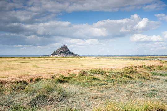 Mont Saint Michel rises from tidal flats under a cloudy sky in Normandy, France, capturing the essence of the historic landscape
