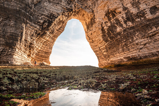 View from inside a sea cave in Normandy looking toward the sky through a chalk arch with weathered rock formations