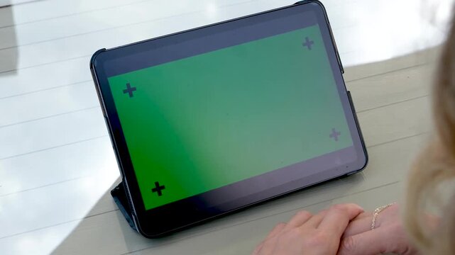 Hands holding a large tablet in horizontal orientation with green screen chroma key for movie watching or website demonstration while sitting outdoors during a sunny bright day