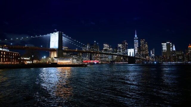 Brooklyn Bridge and Lower Manhattan skyline at night. Illuminated Brooklyn Bridge and Lower Manhattan skyscrapers with Jane's Carousel visible from the waterfront at night.