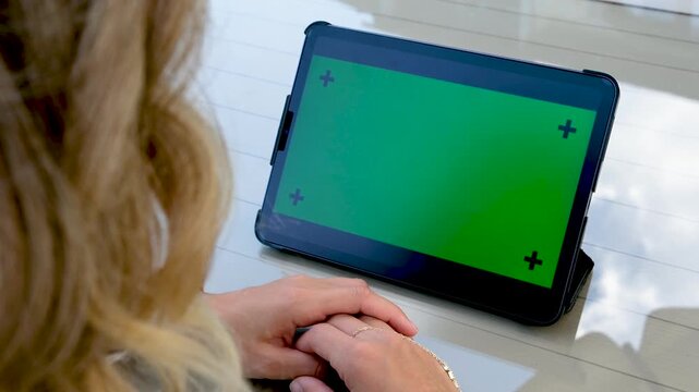 Close up of hands holding a tablet computer with green screen chroma key and markers for motion tracking while sitting outdoors at a wooden table for digital product demo session