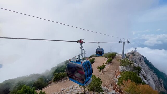 Cable car cabins moving above a mountain ridge and clouds at Mount Babadag in Mugla Turkey. Aerial cable transport over rocky slopes at high altitude used for sightseeing