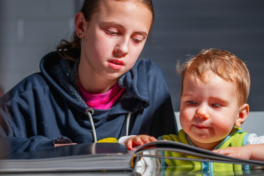 Natural unposed scene of older sister reading with her toddler brother, expressing real emotions, calm interaction, and authentic home learning environment.