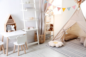 Stylish toy wigwam, furniture, pillows and decor in light playroom. Interior design © New Africa