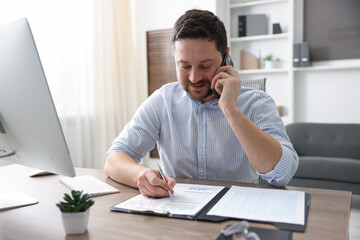 Naklejka premium Man talking on smartphone at wooden desk indoors