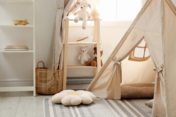 Stylish toy wigwam, furniture, pillows and decor near window in playroom. Interior design © New Africa