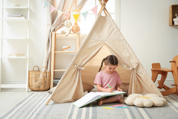 Little girl drawing in sketchbook near toy wigwam at home, space for text © New Africa