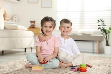 Fototapeta premium Smiling little friends with toy pyramids sitting on floor at home
