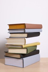 Stack of different books on wooden table against light background