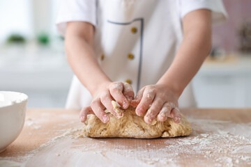 Fototapeta premium Child kneading dough at wooden table indoors, closeup