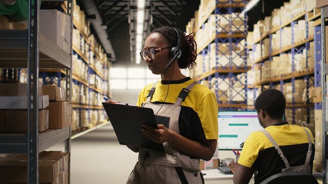 Black female staff answering a customer service call in a logistics hub, assisting with order tracking for parcels, fixing a wrong address issue and updating shipping details. Help line. Camera A.