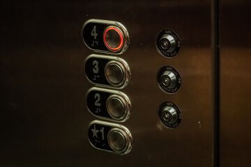 Close-up of a stainless steel elevator control panel featuring braille and numbered buttons with the fourth floor button illuminated in red © Donald