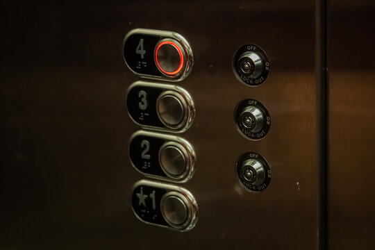 Close-up of a stainless steel elevator control panel featuring braille and numbered buttons with the fourth floor button illuminated in red