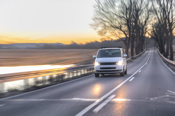 White minivan driving on rural road near river at sunset. Car travel highway. © puhimec