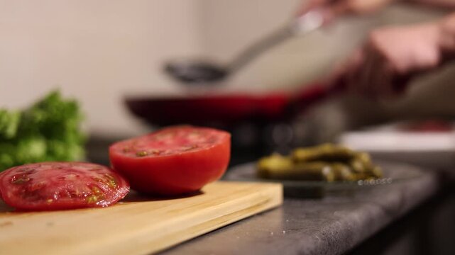 4K defocused video. 60 fps. Tomato in foreground. Chef turns cutlet of ground meat, beef, pork, lamb on frying pan with spatula. Blurred background. Cook flips round burger patty. Lunch, health food