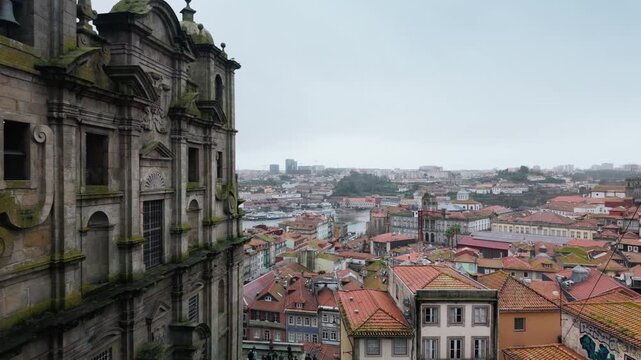 Slow panning shot of Porto's traditional red tile rooftops and the Douro River, starting from the historic Church of Saint Lawrence, revealing the cityscape on an overcast and rainy day