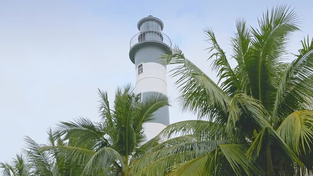 A low angle shot of the historic Cua Dai Lighthouse in Hoi An, Vietnam, surrounded by palm trees against a cloudy sky.