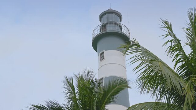 A low angle shot of the historic Cua Dai Lighthouse in Hoi An, Vietnam, surrounded by palm trees against a cloudy sky.