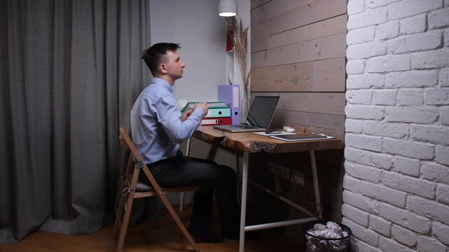 Young man sitting at a desk with a laptop, throwing a crumpled paper ball, distracting himself from work duties and experiencing boredom in home office
