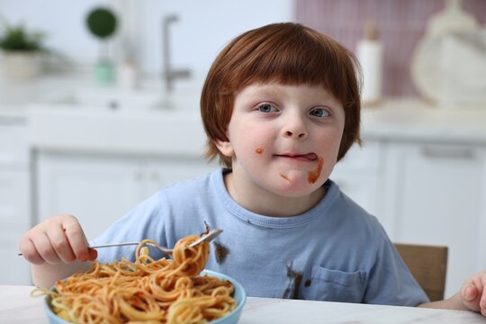 Little boy stained shirt while eating spaghetti at table indoors