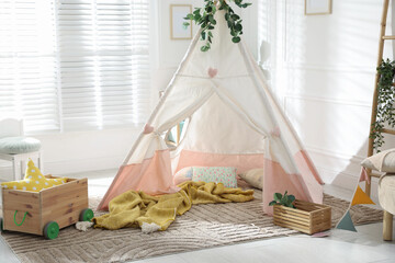 Toy wigwam with pillows, wooden cart, furniture and floral decor in room © New Africa